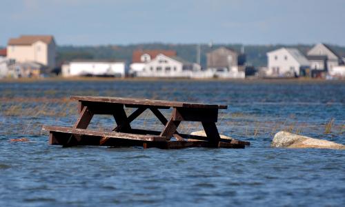 Flooded picnic table with houses in background in Seabrook, NH