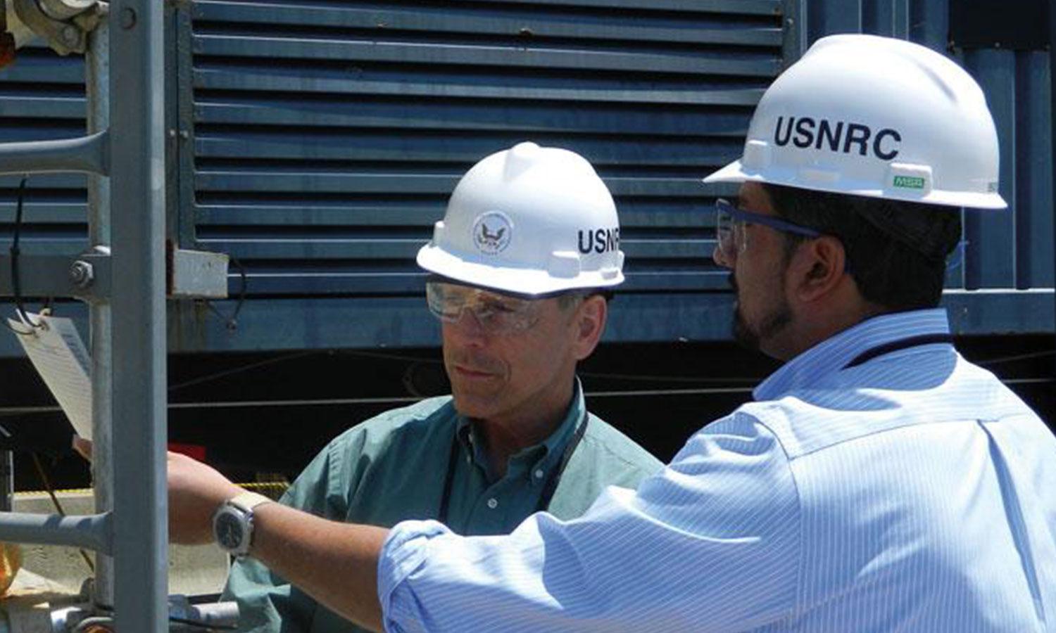 Two men with white USNRC hard hats look at document