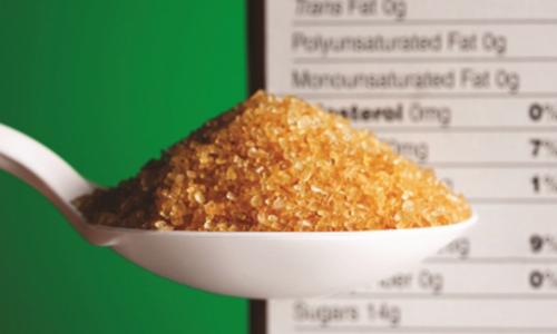 A spoon of raw sugar hovers in front of a cereal box's nutrition facts