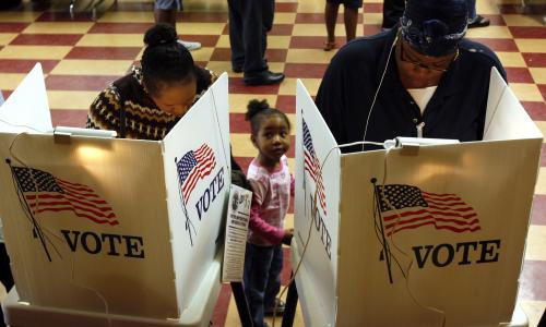 Two adults and a child stand in front of a voting booth