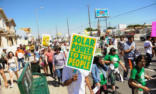 A group of people marching with a sign that reads "Solar power to the people."