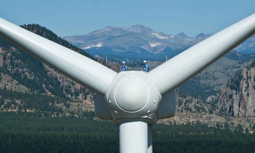 Renewable energy workers on wind turbine with mountains in background