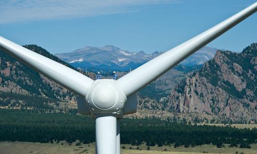 Workers standing on top of a wind turbine with mountains in the background