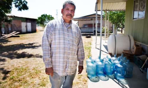 Male San Joaquin Valley community member stands in front of water jugs
