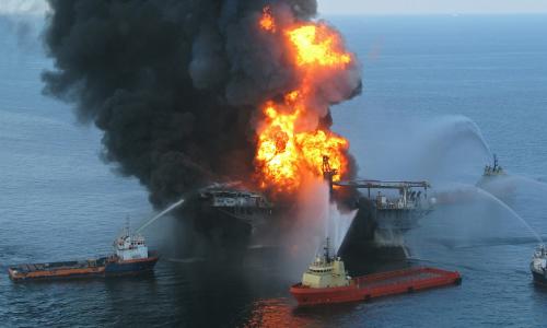 A fleet of ships tries to extinguish a flaming oil rig.