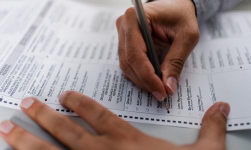 A closeup of a person's hands filling out a ballot.