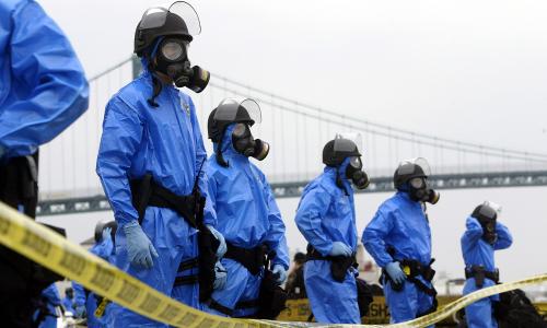 A line of people behind caution tape wearing nuclear contamination suits.