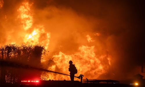 Firefighter standing on fire truck hosing down huge fire